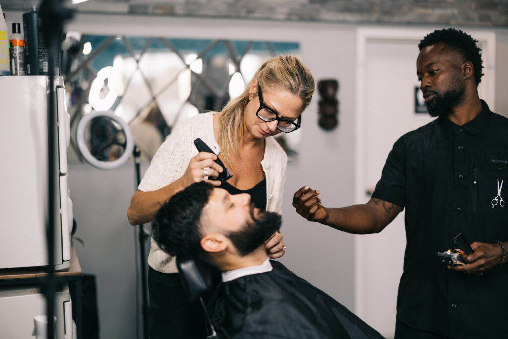 Instructor William Biney watching a QC Barber Academy student trim a client's beard